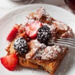 French Toast Casserole on a white circle plate with a fork cutting into it.