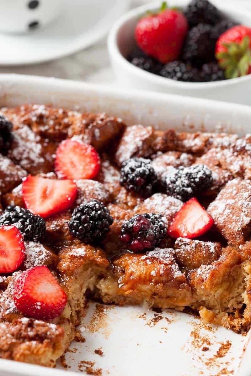 White casserole dish full of baked french toast casserole with one piece already cut out.