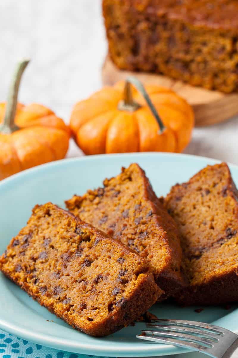 Slices of Moist Pumpkin Bread on a blue plate with mini pumpkins in the background.