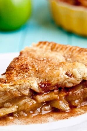Apple pie with flaky butter crust sliced on a white plate.