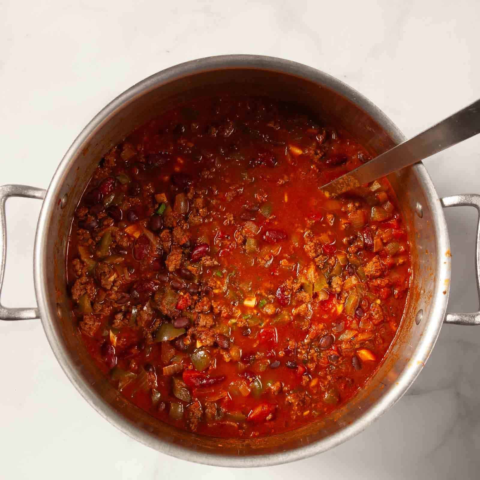 Adding the tomatoes and other ingredients to make the stovetop chili.