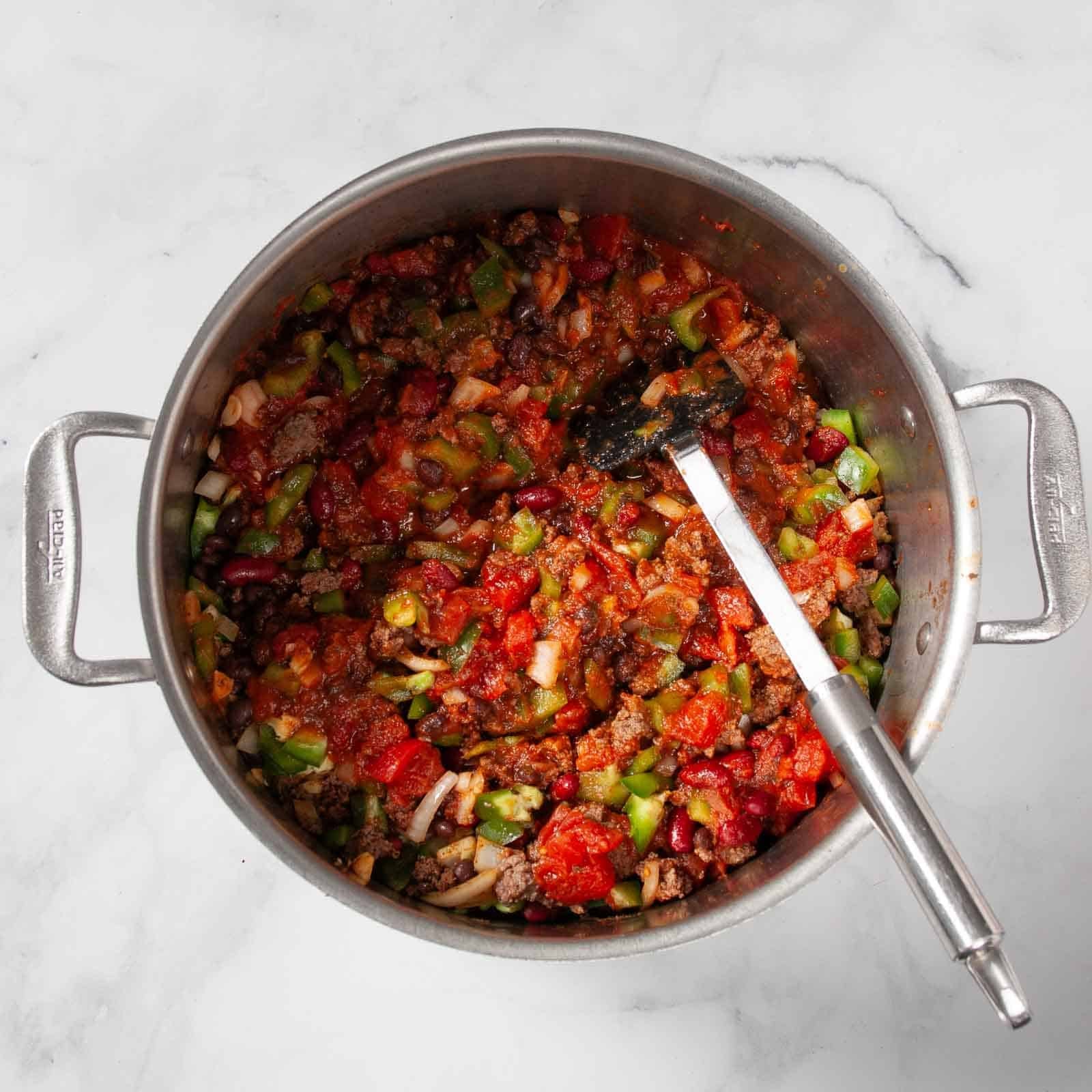 Stirring together all the chili ingredients in a large pot.