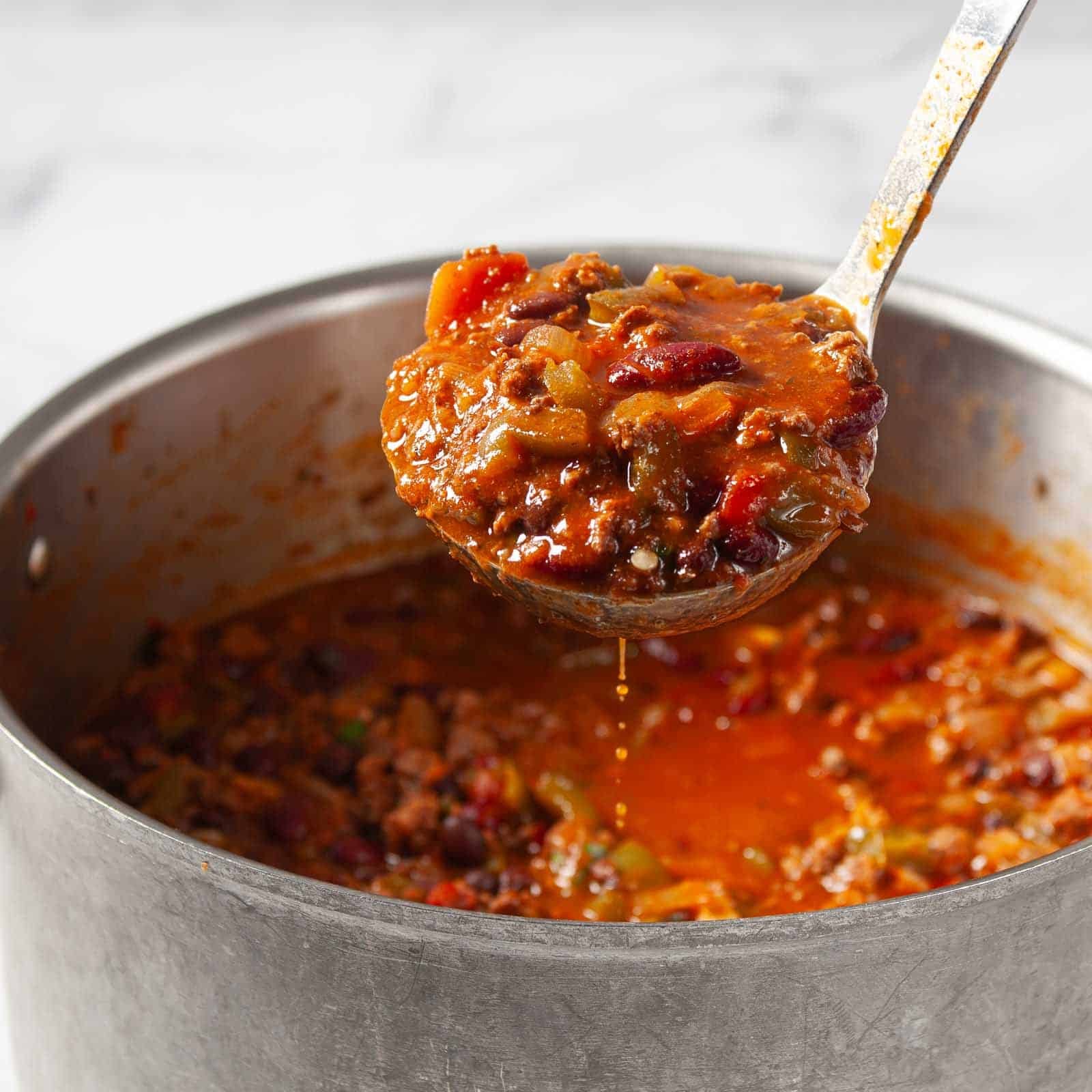 A soup ladle scooping out a heaping serving of stovetop chili.