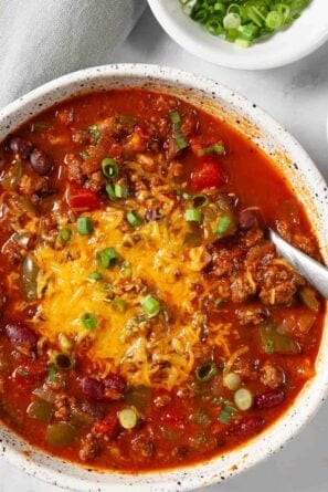 Adding toppings onto a white bowl full of homemade chili.