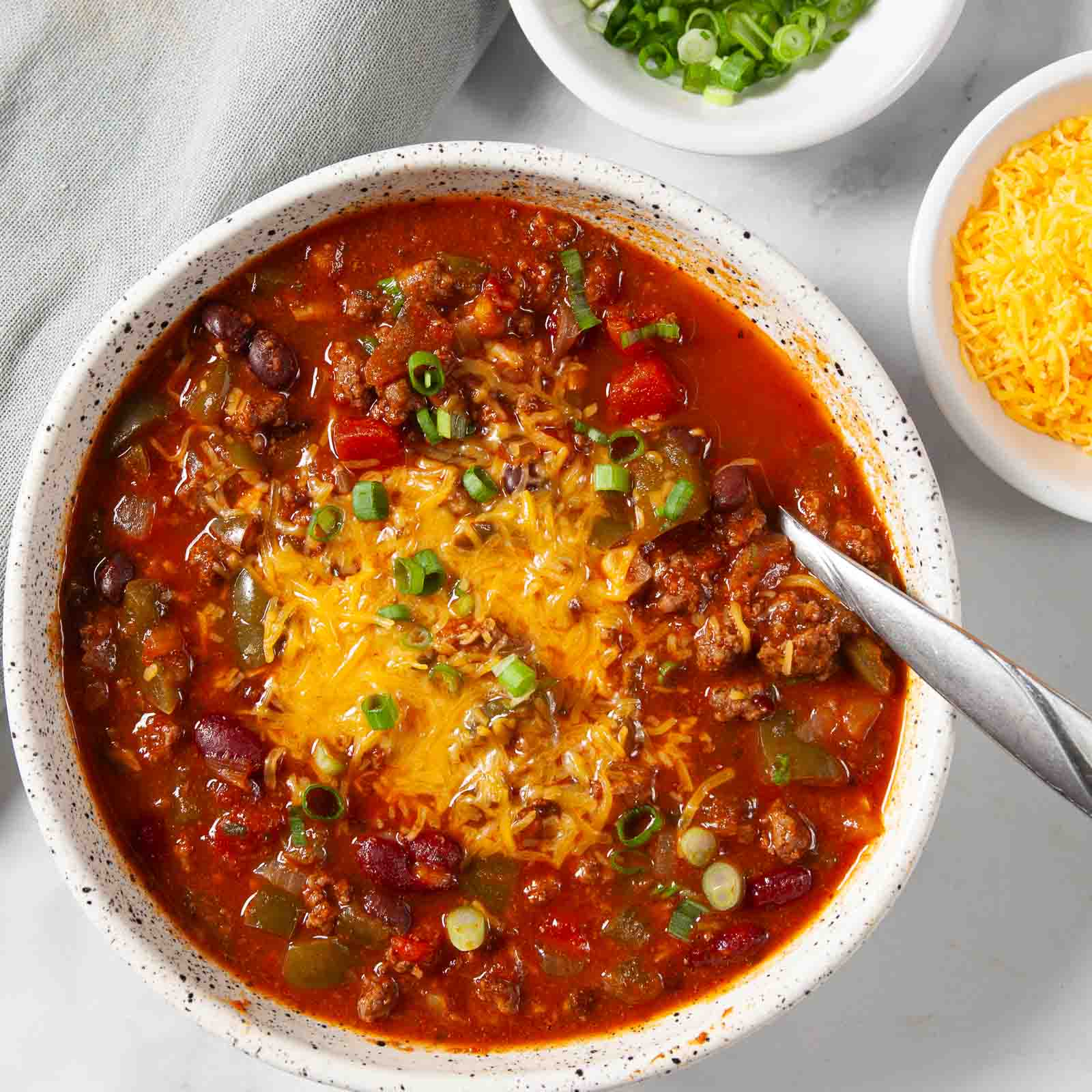 Adding toppings onto a white bowl full of homemade chili.