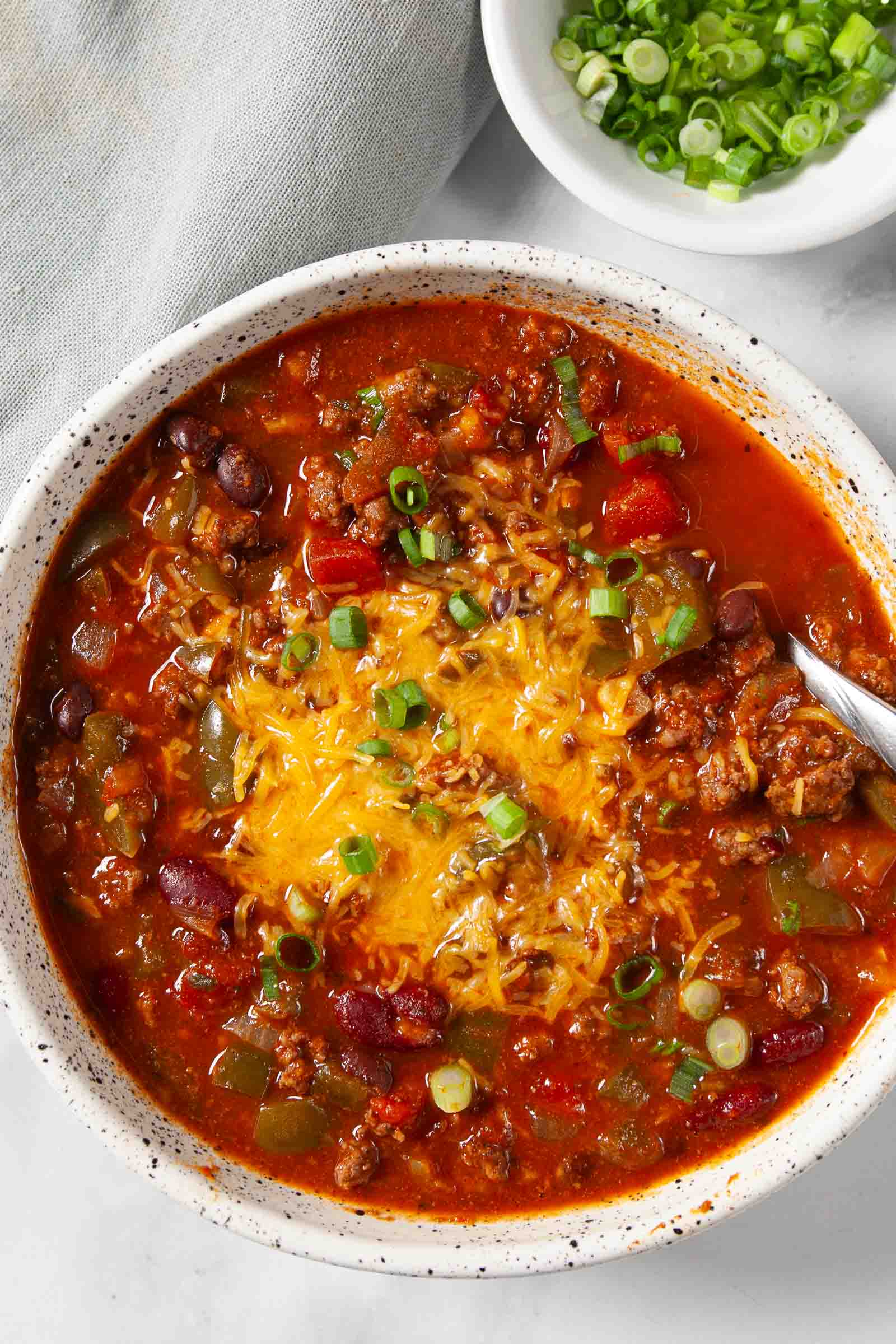 White bowl full of classic chili and toppings.