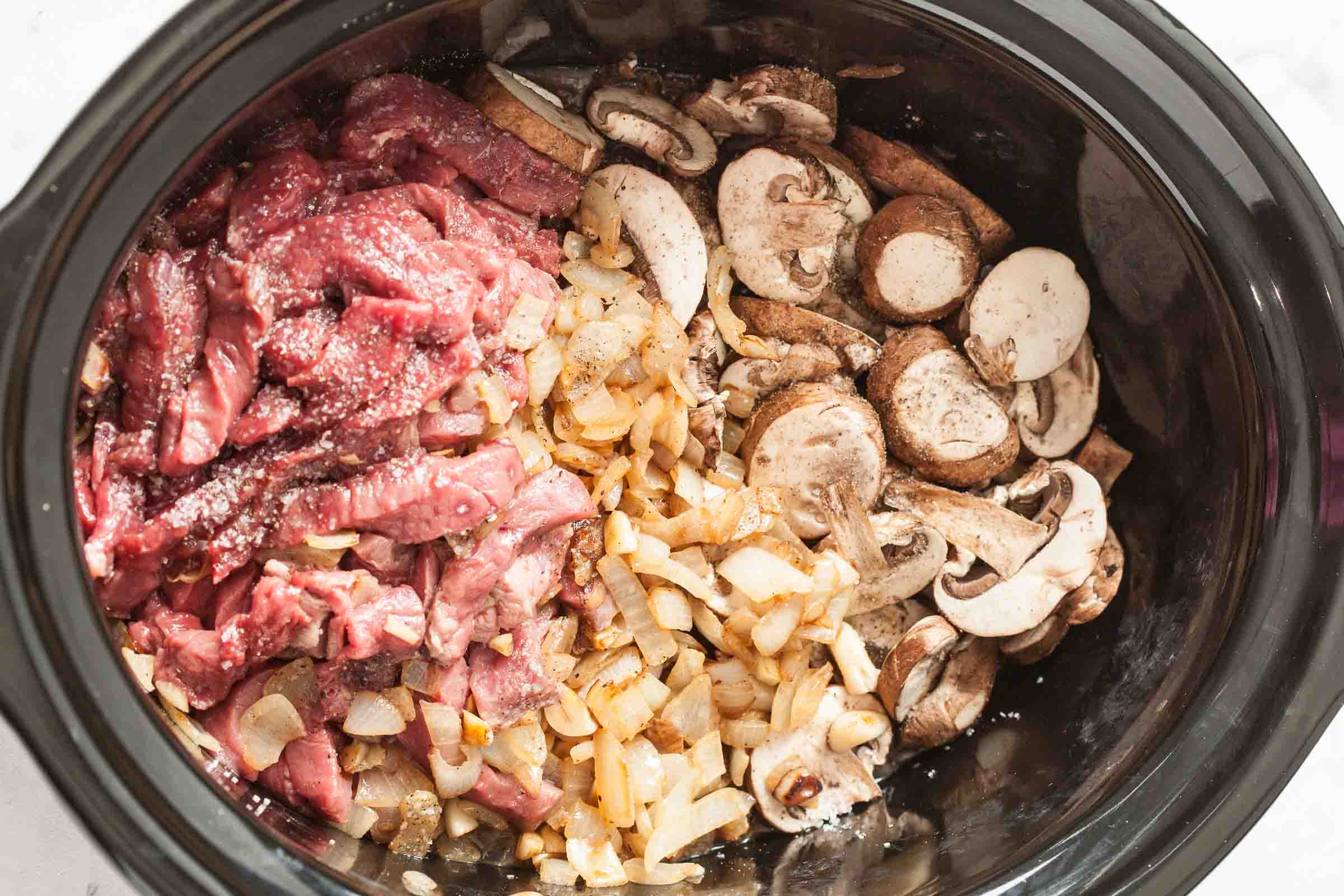 Adding the ingredients into the slow cooker to make the Crockpot Beef Stroganoff.