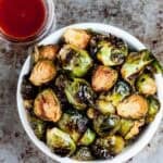Square feature image of a white bowl full of Oven Roasted Brussels Sprouts.