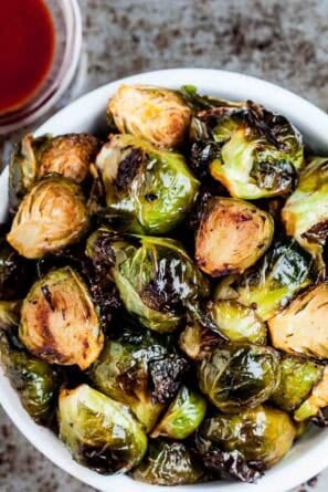 Square feature image of a white bowl full of Oven Roasted Brussels Sprouts.